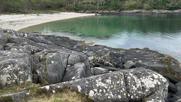 A rocky shoreline with a sandy beach and a calm body of water.