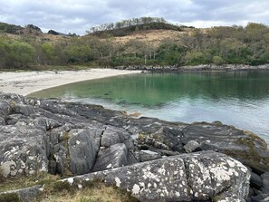 A rocky shoreline with a sandy beach and a calm body of water. - Clearwater House (Lochailort)