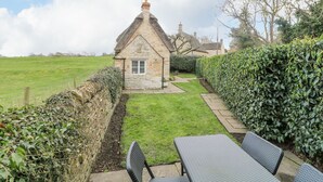 A stone cottage with a thatched roof, a small garden, and a paved pathway leading to a table and chairs. - Bumble Bee (Oakham)