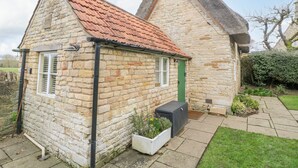 A stone cottage with a red-tiled roof, a green door, and a small garden area with a planter and a pathway. - Bumble Bee (Oakham)