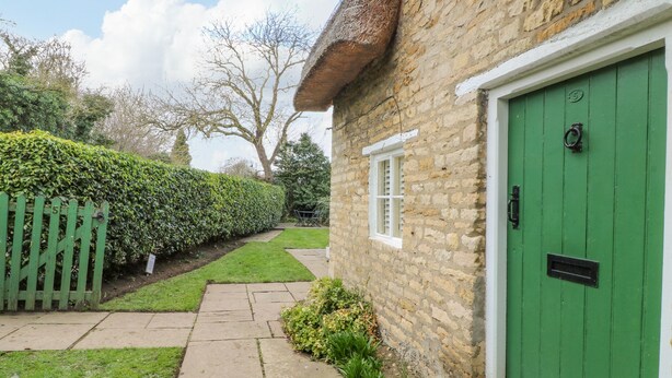 A stone house with a green door, a stone pathway, and a neatly trimmed hedge. - Bumble Bee (Oakham)