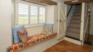 A room with a built-in bench with colorful cushions, a door leading to a staircase, and a window with shutters. - Bumble Bee (Oakham)
