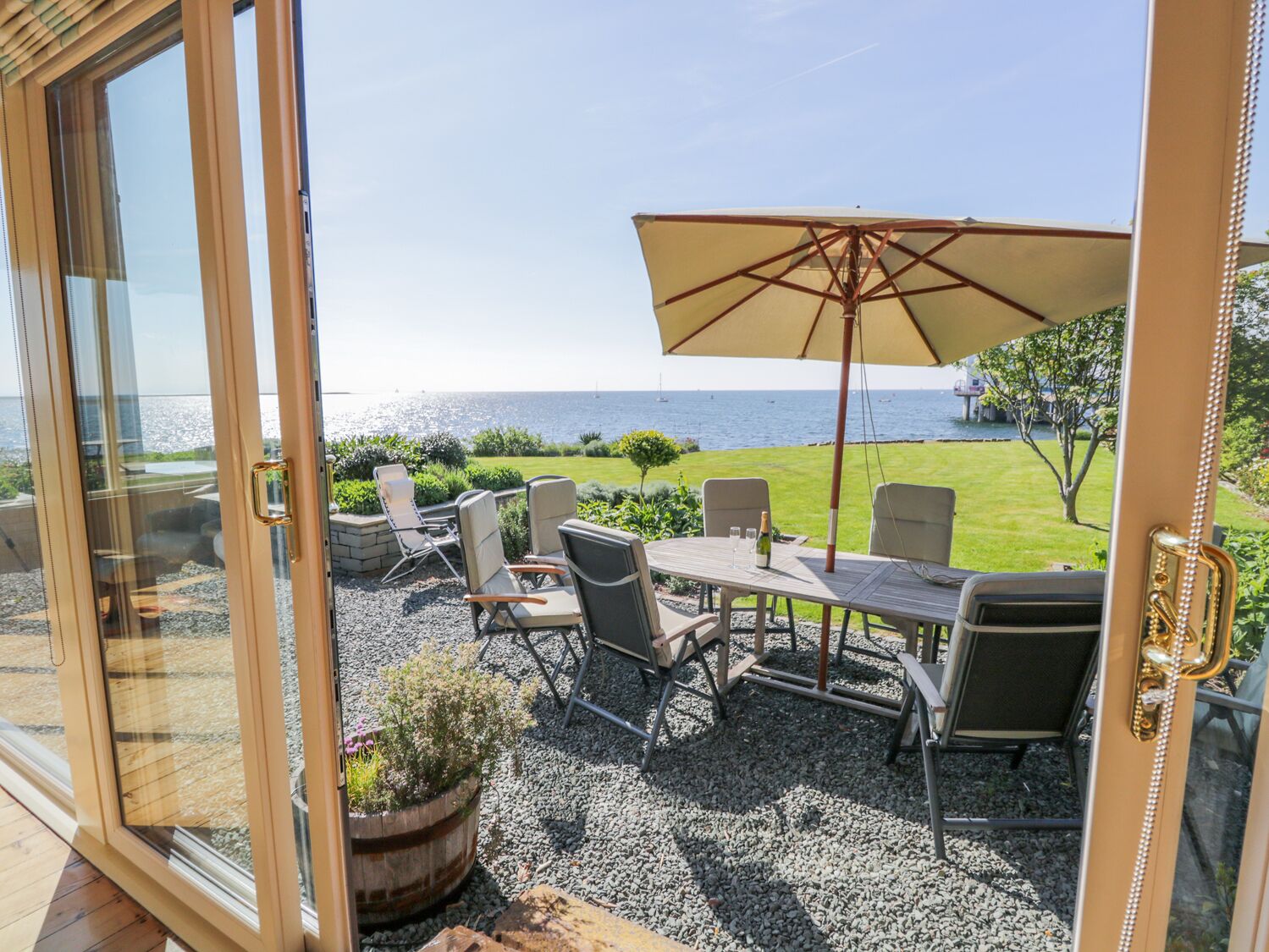 A patio with a table and chairs, a large umbrella, and a view of the sea.
