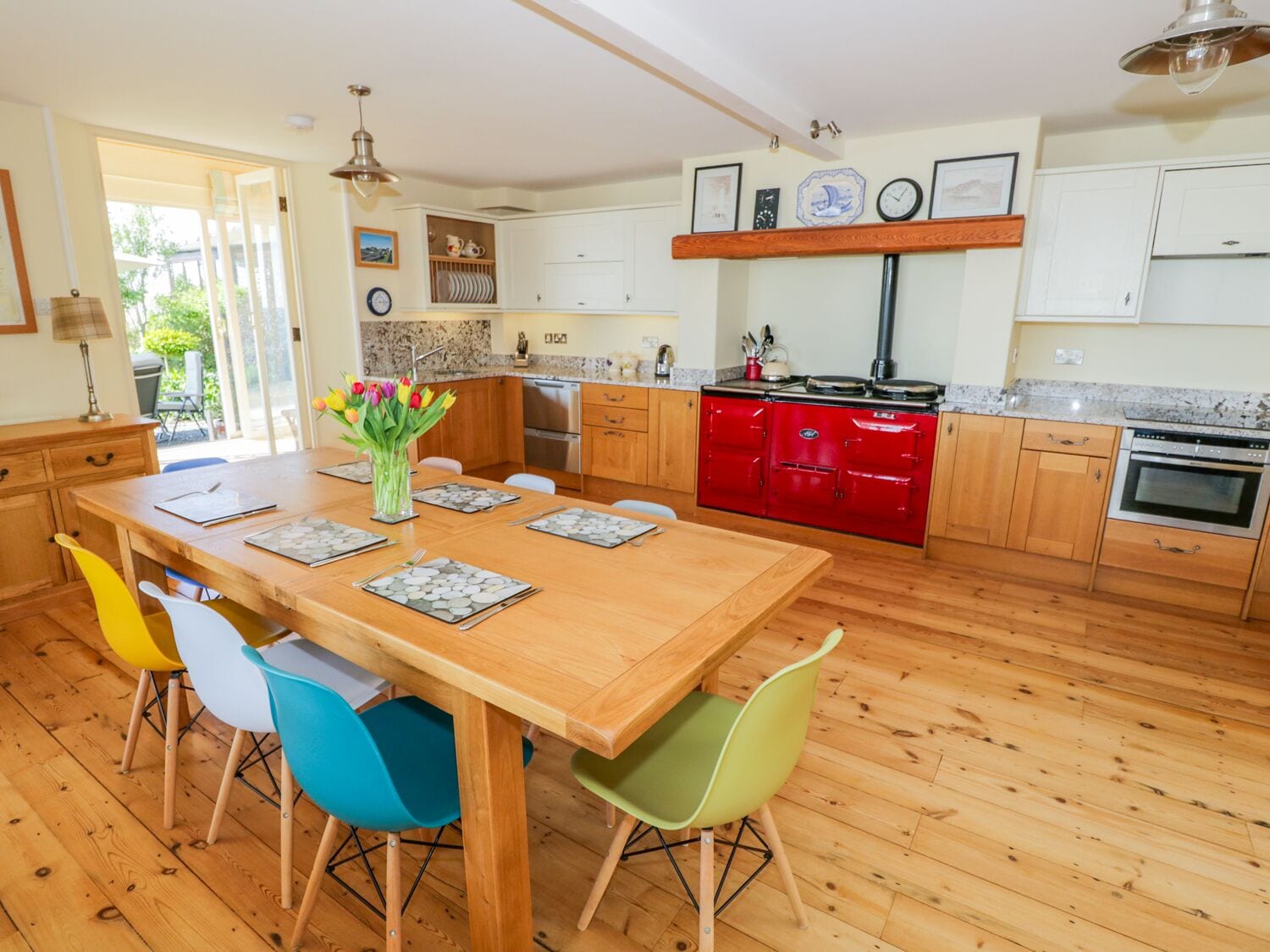 Une cuisine moderne avec un plancher en bois, un îlot central doté de chaises, un poêle rouge et une table à manger pour quatre personnes.
