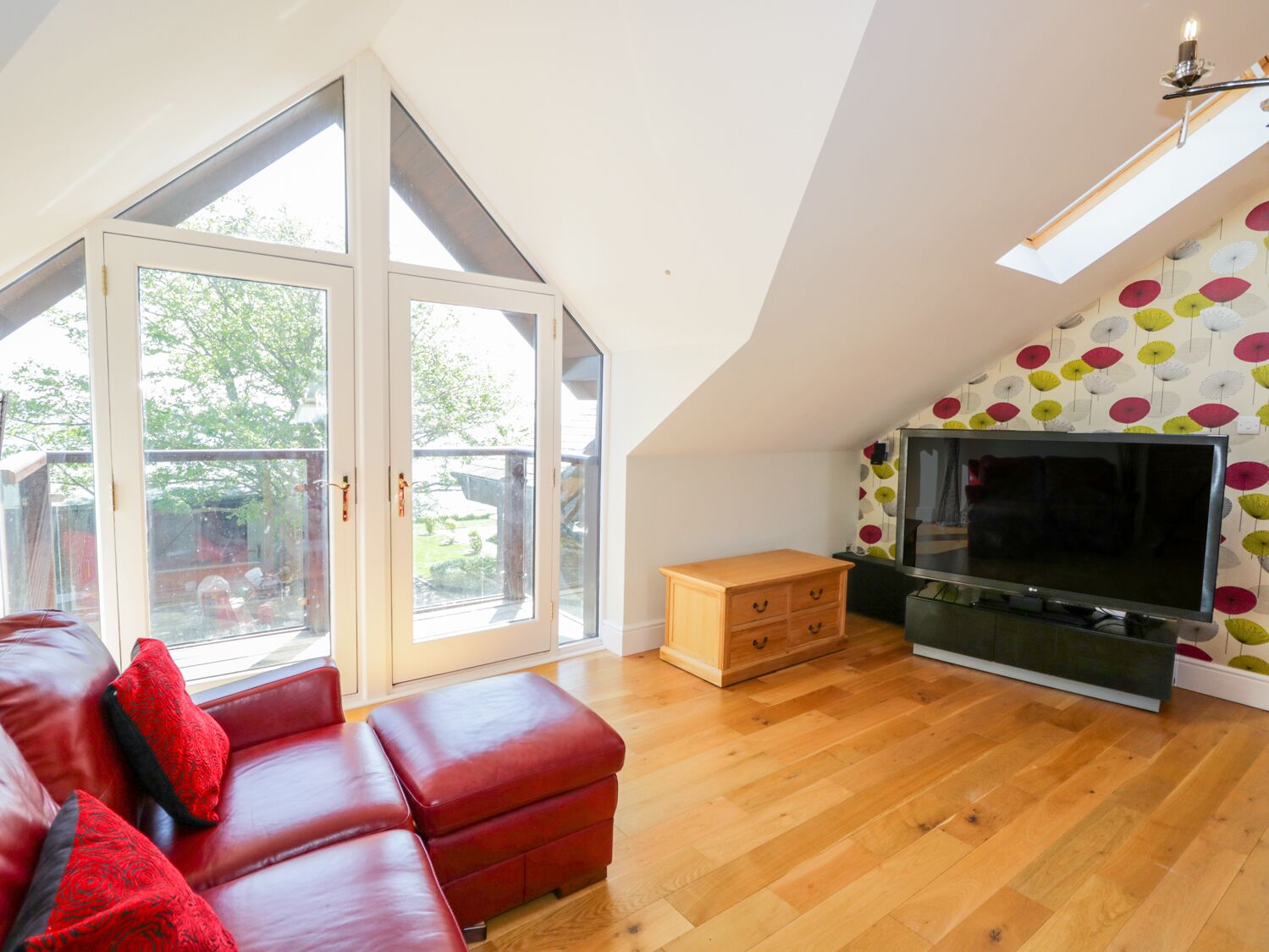 A spacious living room with a red leather sofa, a wooden cabinet, and a television.