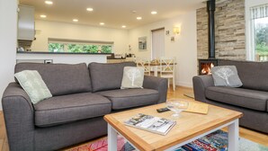 Uma sala de estar moderna com dois sofás cinzentos, uma mesa de centro de madeira com revistas e uma lareira.