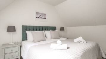 A neatly made bed with a green headboard, two bedside lamps, and a small bedside table with a lamp and a glass.