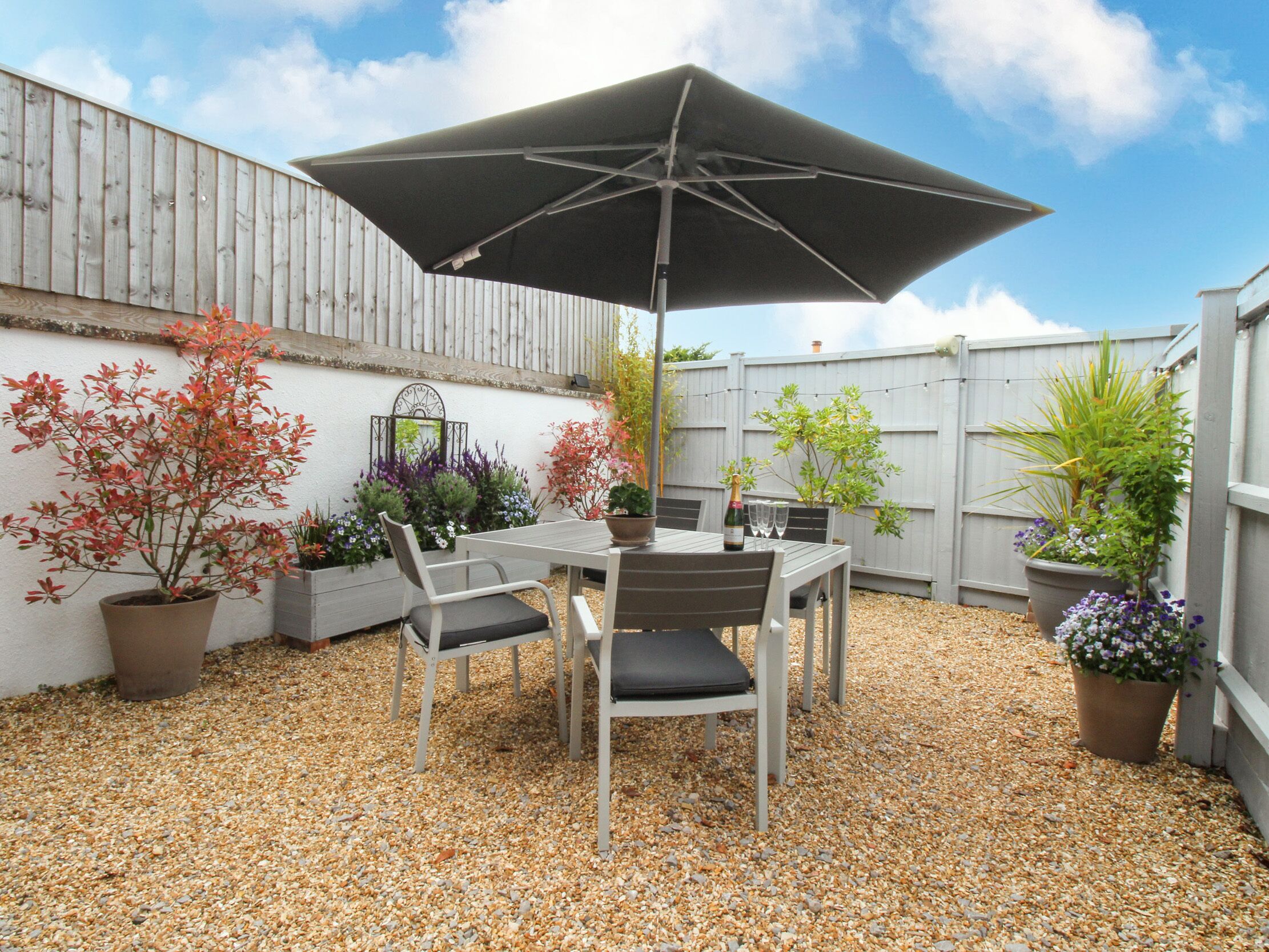 A patio with a table and chairs, an umbrella, and potted plants.