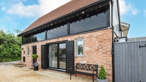 A brick house with a large sliding glass door, a bench, and a small potted plant. - Meadow View Barn (Wareham)