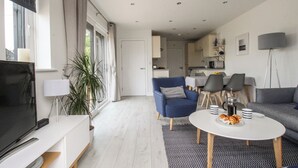 A modern living room with a flat-screen TV, a sofa, a blue armchair, and a dining area with a table and chairs. - Meadow View Barn (Wareham)