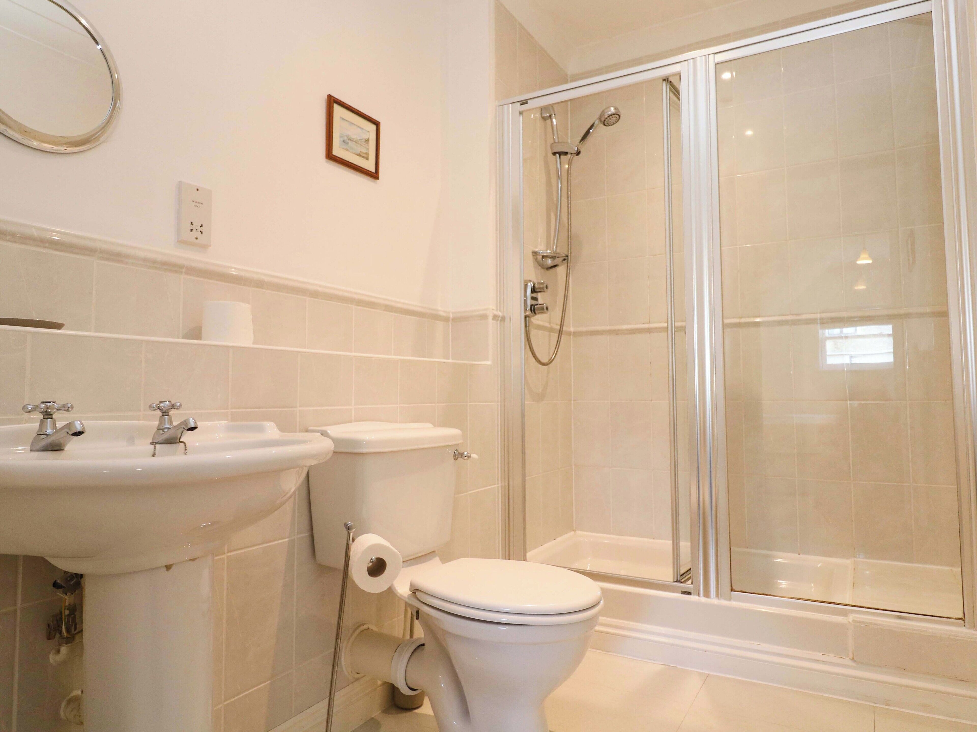 Un baño con lavamanos, inodoro y ducha con mampara de vidrio.