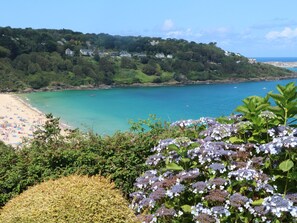A coastal landscape with a beach, clear turquoise waters, and lush greenery. - Meridian (St Ives)