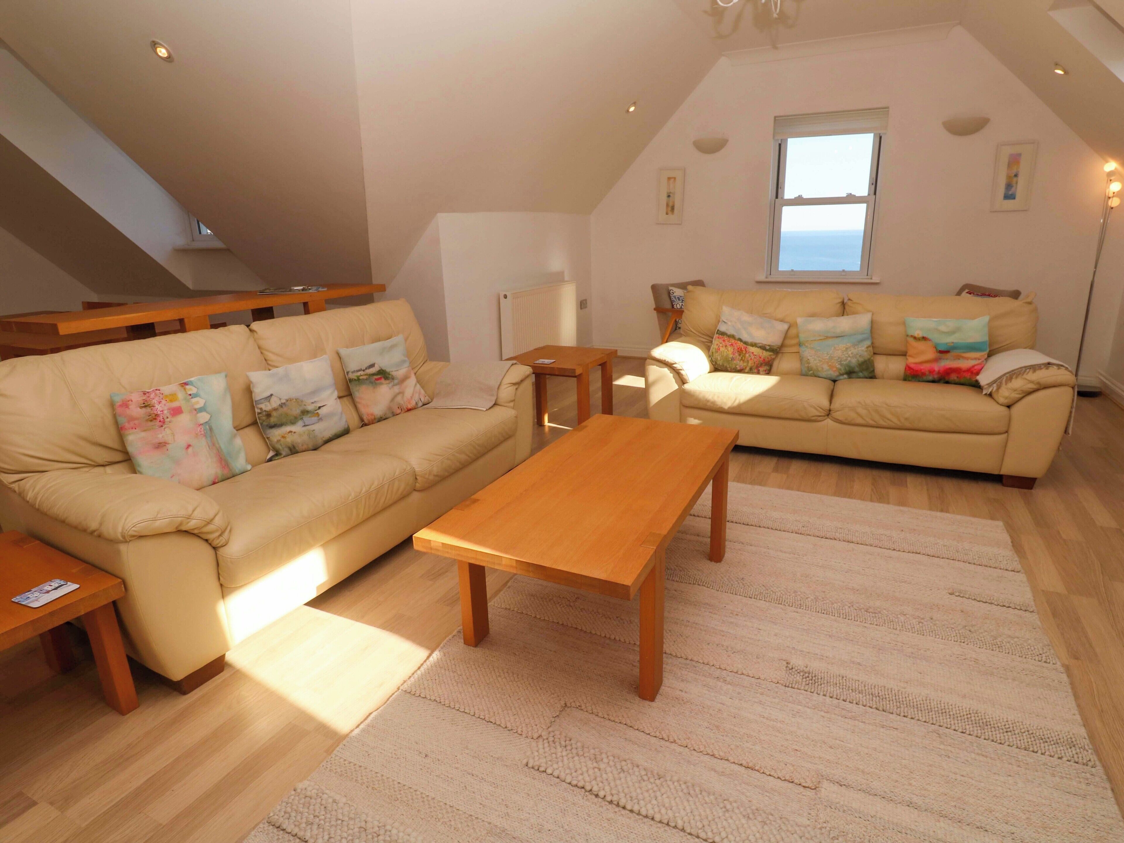 A spacious living room with a high ceiling, a large window offering a view, a beige sofa, a wooden coffee table, and a small wooden side table.