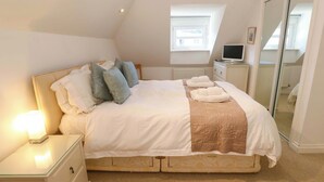 A neatly made bed with pillows, a bedside lamp, and a TV on a bedside table. - Meridian (St Ives)