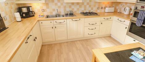 A kitchen with light-colored cabinets, a wooden countertop, a gas stove, a toaster, and a coffee maker.