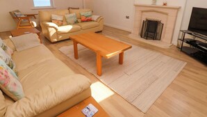 A spacious living room with a sofa, a wooden coffee table, and a fireplace. - Meridian (St Ives)