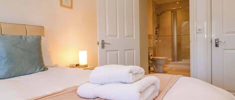 A hotel room with a bed, a bedside lamp, a framed picture on the wall, and a bathroom visible through an open door.