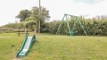 A playground with a slide and swings in a grassy area.