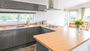 A modern kitchen with a central island, grey cabinets, and a large window providing natural light. - Alder Lodge (Newton Abbot)