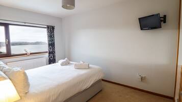 Habitación de hotel con cama, televisión en la pared, ventana con cortinas y vista al mar.
