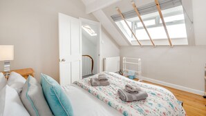 A bedroom with a skylight, a bed with floral bedding, and a bedside table with a lamp. - Salty Fox (Whitby)