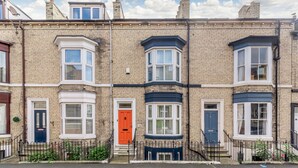 A row of terraced houses with bay windows, a red door, and a black metal fence. - Salty Fox (Whitby)