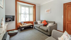 A living room with a grey sofa, a wooden coffee table, a TV, and a window with curtains. - Salty Fox (Whitby)