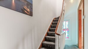 A staircase with carpeted steps and a wooden handrail, leading to a room with a door and a window with colorful window shades. - Salty Fox (Whitby)