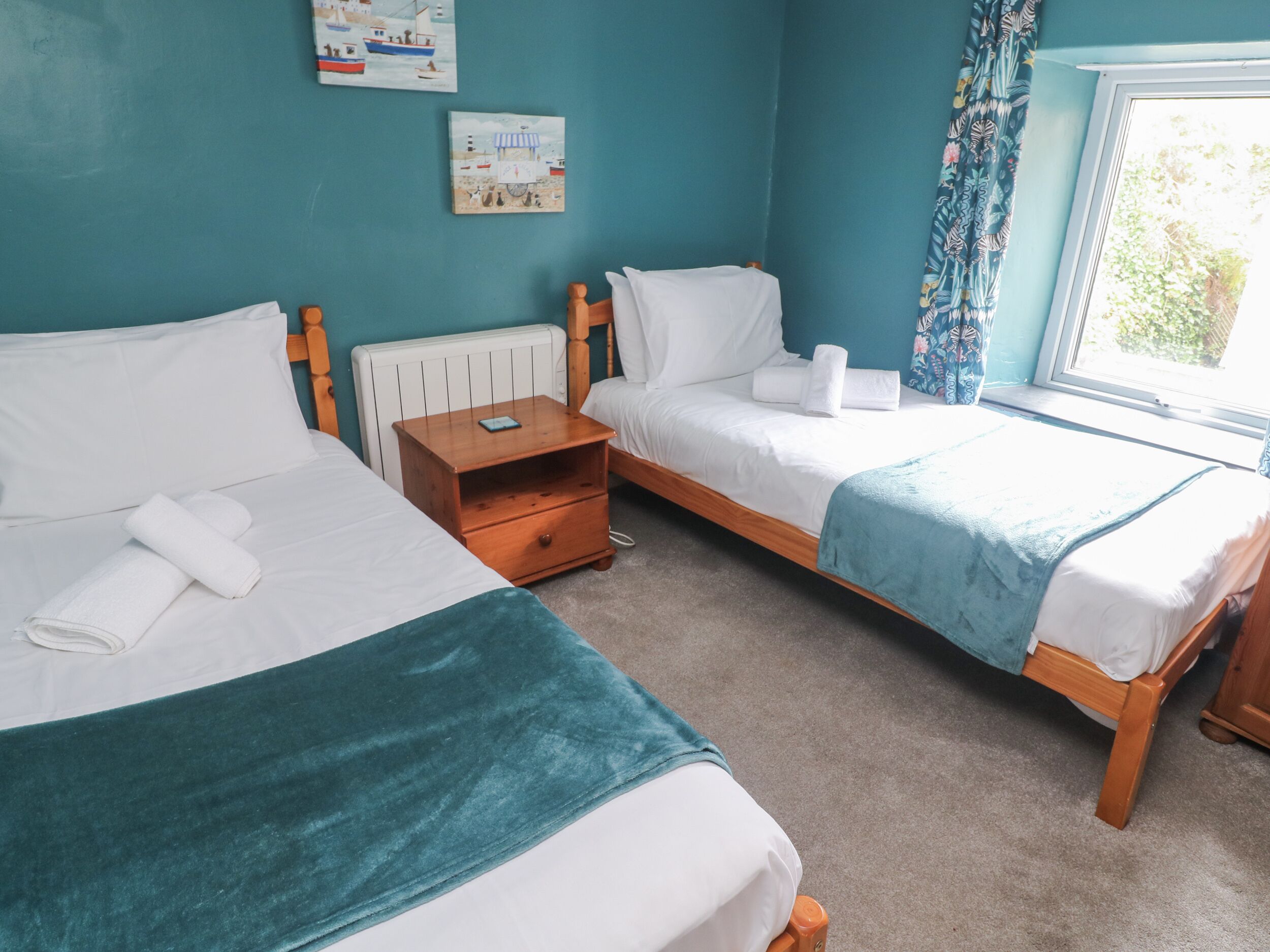 A bedroom with two beds, a wooden nightstand, and a window with curtains.