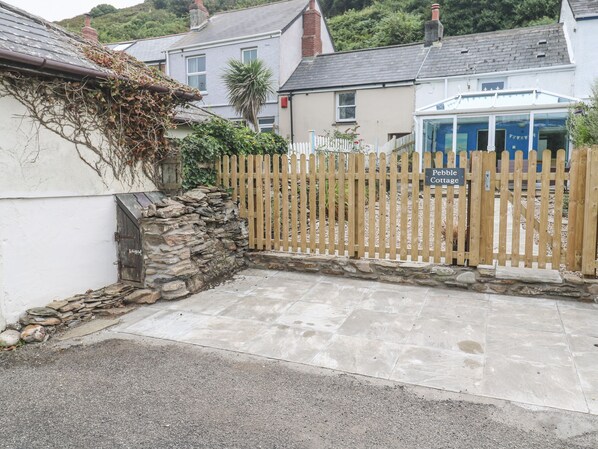 Un muro de piedra, una valla de madera y un edificio con el letrero 'Pebble Cottage'.