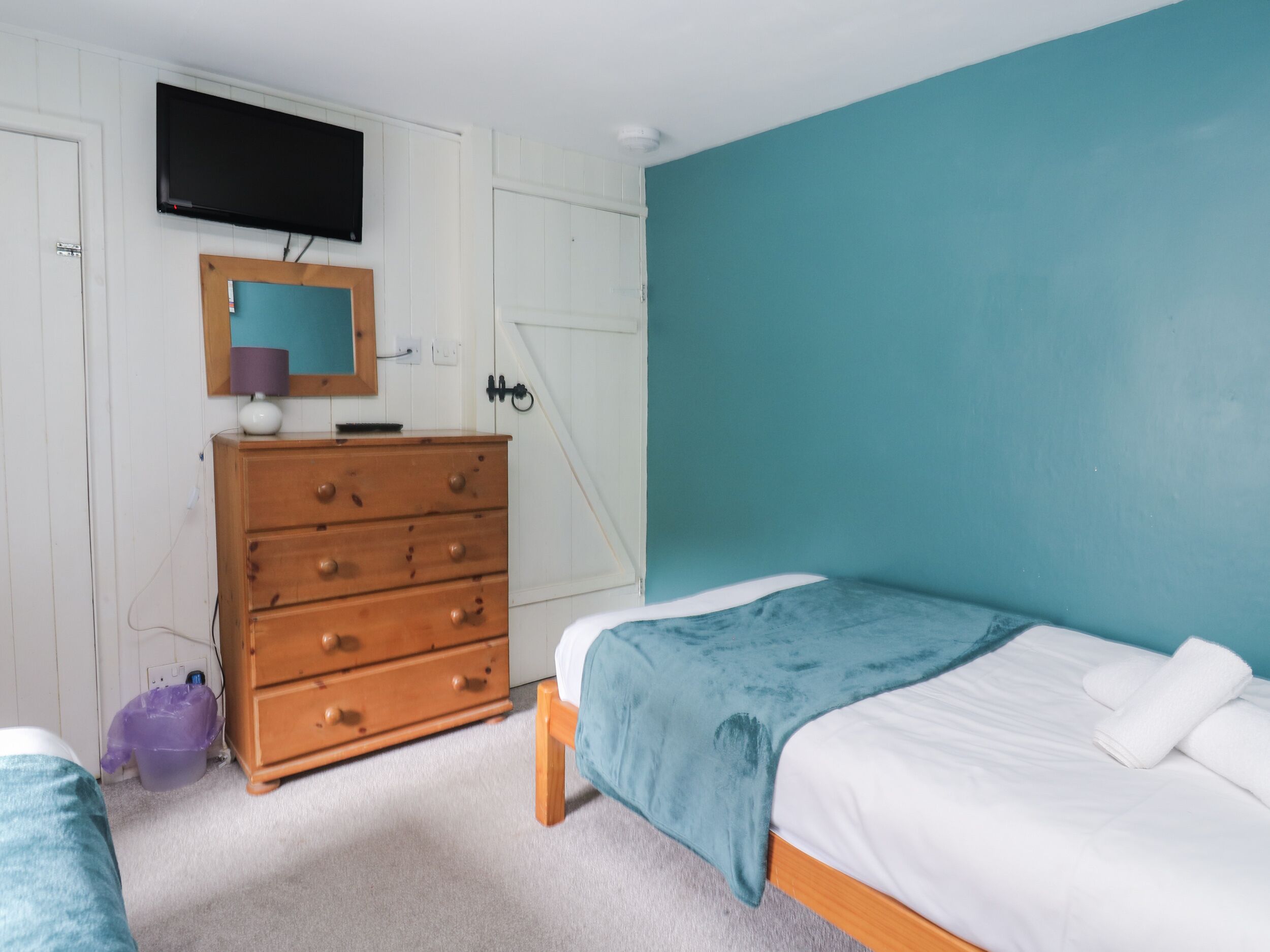 Un dormitorio con cama, cómoda, televisor y pared color esmeralda.