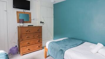 A bedroom with a bed, a dresser, a television, and a teal wall.