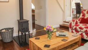 A cozy living room with a wood-burning stove, a sofa with a red leaf pattern, a wooden coffee table with a vase of flowers, and a staircase leading to another room.