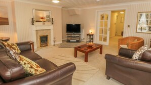 A living room with a fireplace, leather sofas, a television, and a door leading to another room. - The Garden Apartment (Filey)