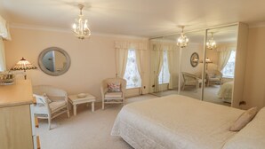 A bedroom with a large bed, a dresser, a chair, a mirror, and a chandelier. - The Garden Apartment (Filey)