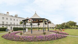 A gazebo with a circular flower bed in the center, surrounded by a well-maintained lawn and a building in the background. - The Garden Apartment (Filey)