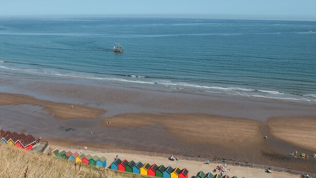 A beach with colorful beach huts and a ship in the distance. - Grays Cottage (Whitby)