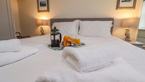 A neatly made bed with white linens, a tray with croissants and orange juice, and two bedside lamps. - Grays Cottage (Whitby)