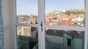 A view from a window with a metal railing, overlooking a town with red-roofed buildings and a hill with a castle-like structure. - Grays Cottage (Whitby)