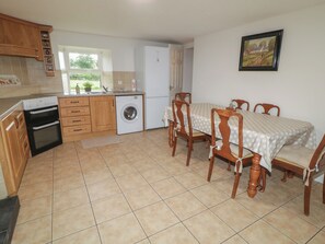 A kitchen with a washing machine, a dining table with chairs, and a window with a view of greenery. - Shaws Hill Farmhouse (Ballymena)