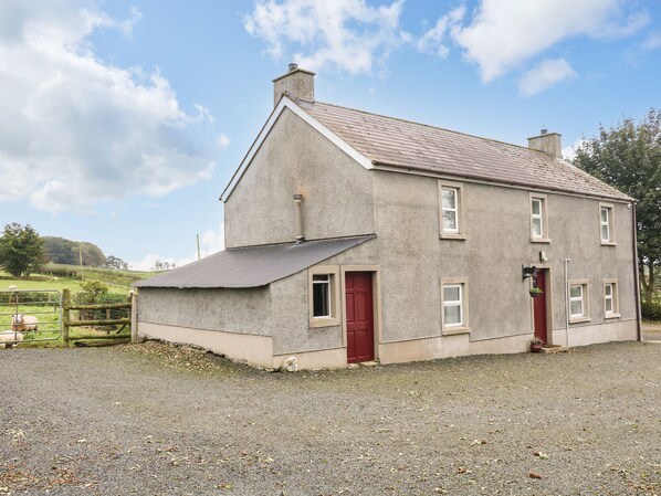 A two-story house with a sloped roof, a red door, and a small porch. - Shaws Hill Farmhouse (Ballymena)