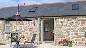 Un bâtiment en pierre avec un toit en tuiles, un patio comprenant une table et des chaises, et des plantes en pot.