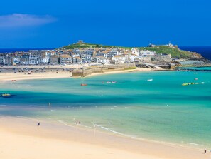 A coastal town with a beach, clear blue waters, and a hilltop building. - An Gwel (Penzance)