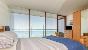 A bedroom with a large bed, a TV, a wardrobe, and a view of the sea through large windows. - The Lookout (Bideford)
