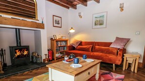 Een gezellige woonkamer met een open haard, een bank, een bijzettafeltje en een boekenkast.