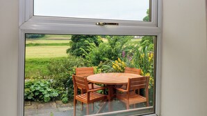 Een raam met uitzicht op een tuin en een houten tafel met stoelen.