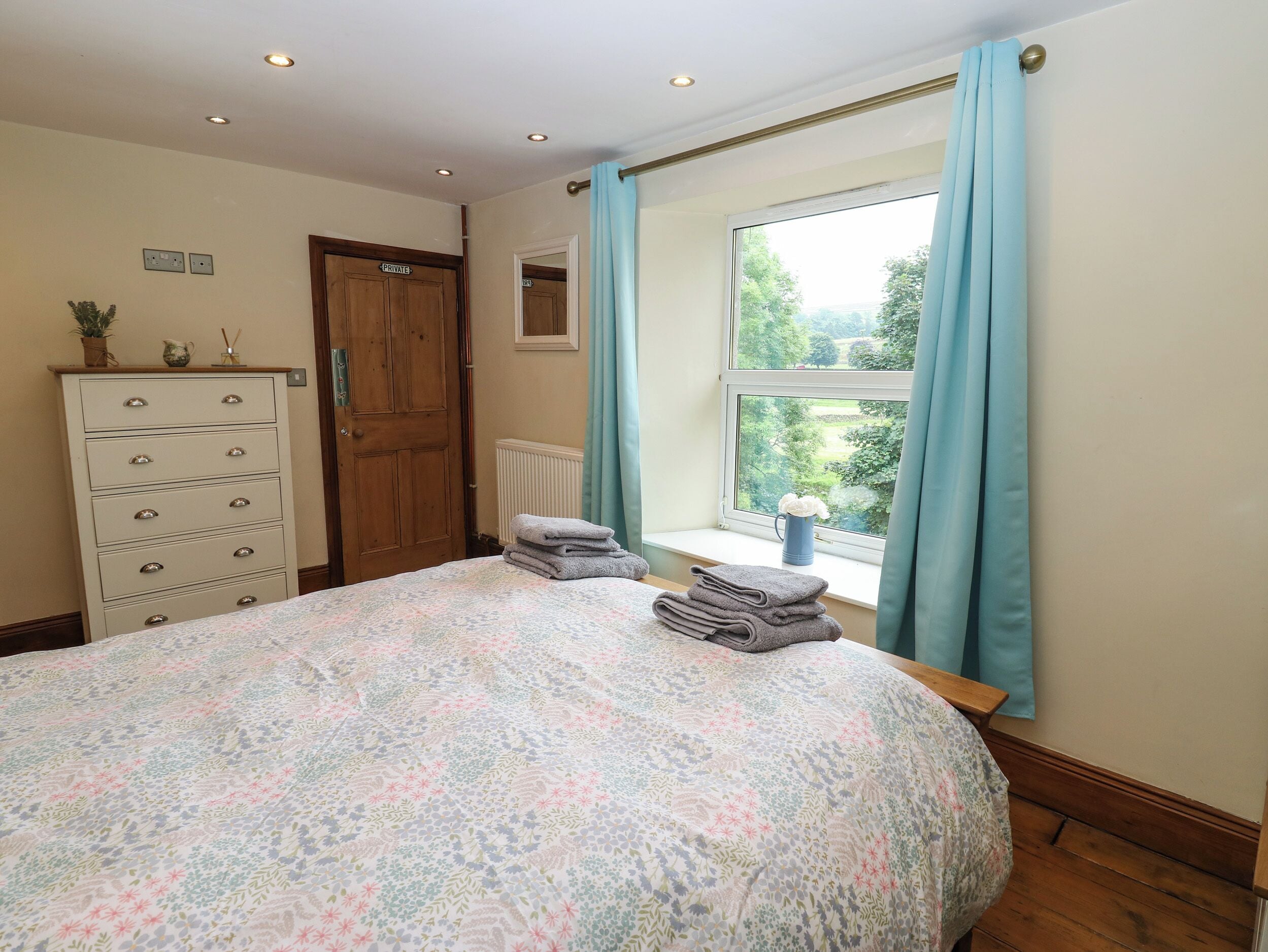 A bedroom with a bed, a dresser, a window with curtains, and a view of greenery outside.