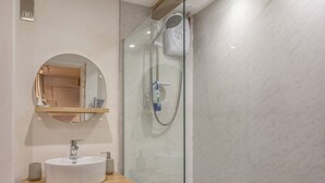 Un baño moderno con un espejo redondo, un lavamanos blanco y una zona de ducha con mampara de vidrio.