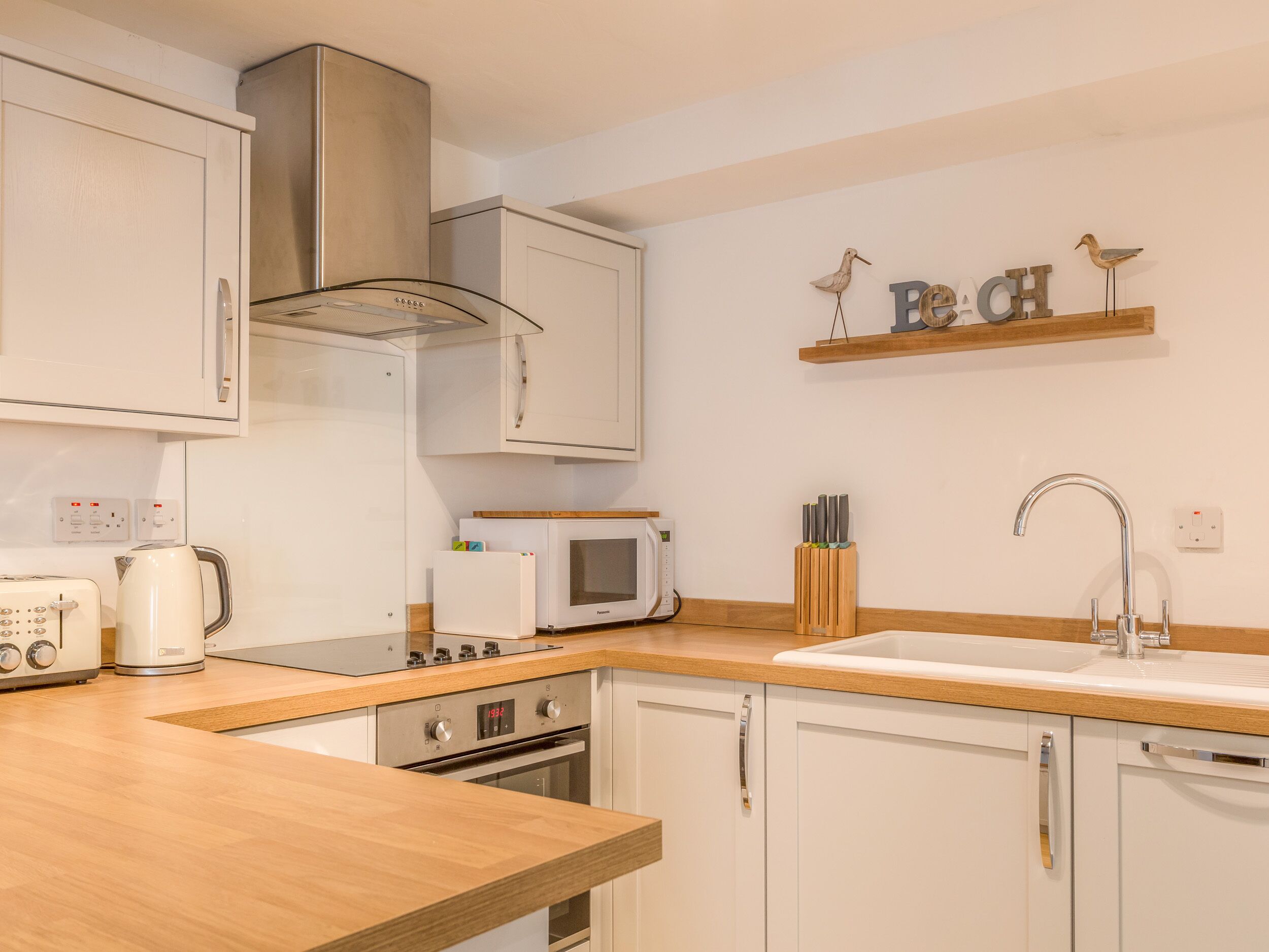A modern kitchen with white cabinets, a microwave, a stove, and a sink. There are decorative bird figures on a shelf above the sink.