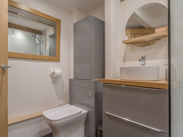 A modern bathroom with a toilet, a mirror, a sink, and a cabinet. - Potters by the Sea (Penzance)